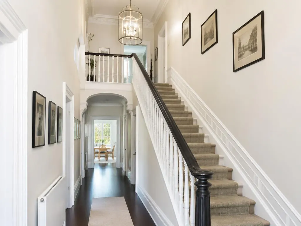 Hallway with a carpeted staircase, white balustrade, framed prints and light cream walls