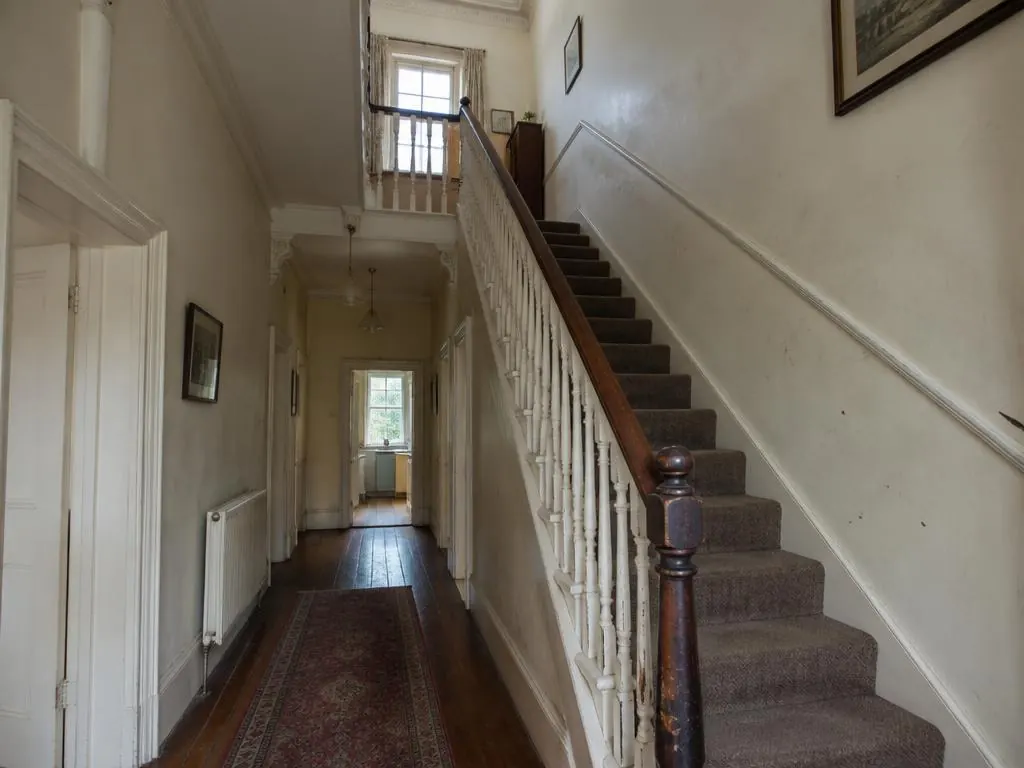 Hallway with a carpeted staircase, white balustrade and marked cream walls