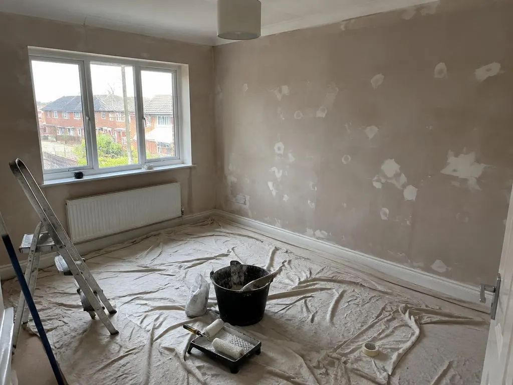 Bedroom with patched walls, dust sheets on the floor, a stepladder and a paint tray
