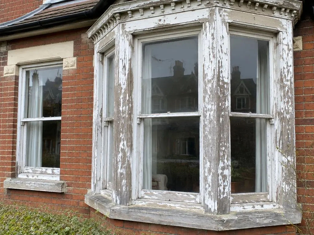 Bay sash window with flaking white paint on a red brick house