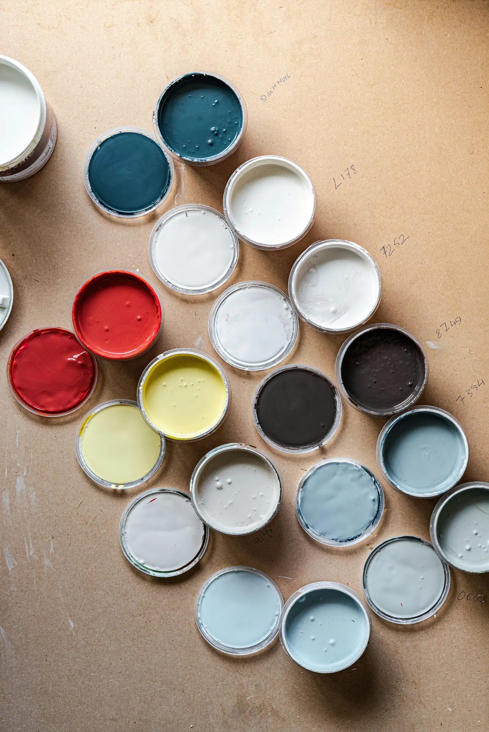 Overhead view of open tester pots of paint in blues, greys, yellow and red on a sheet of cardboard